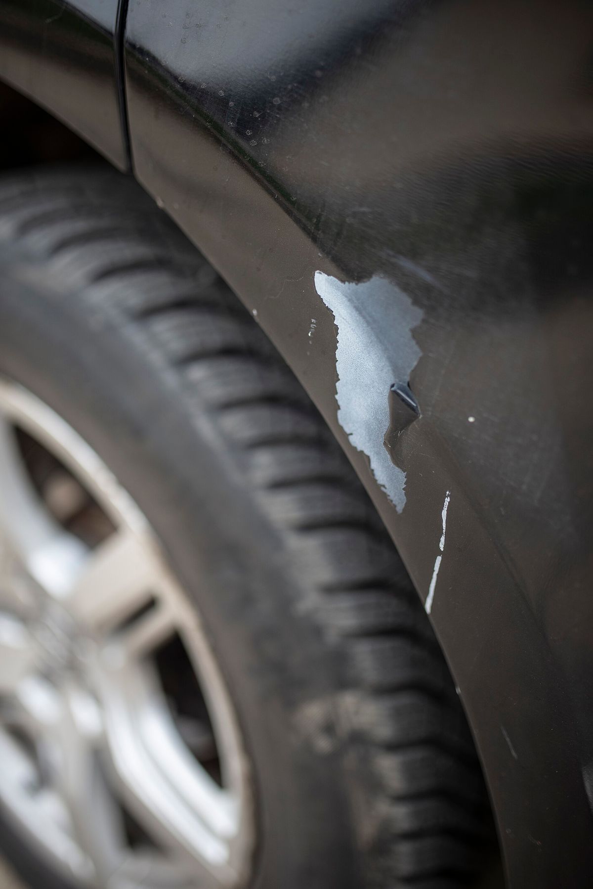 Deep scratches and missing paint along a car fender in a parking lot
